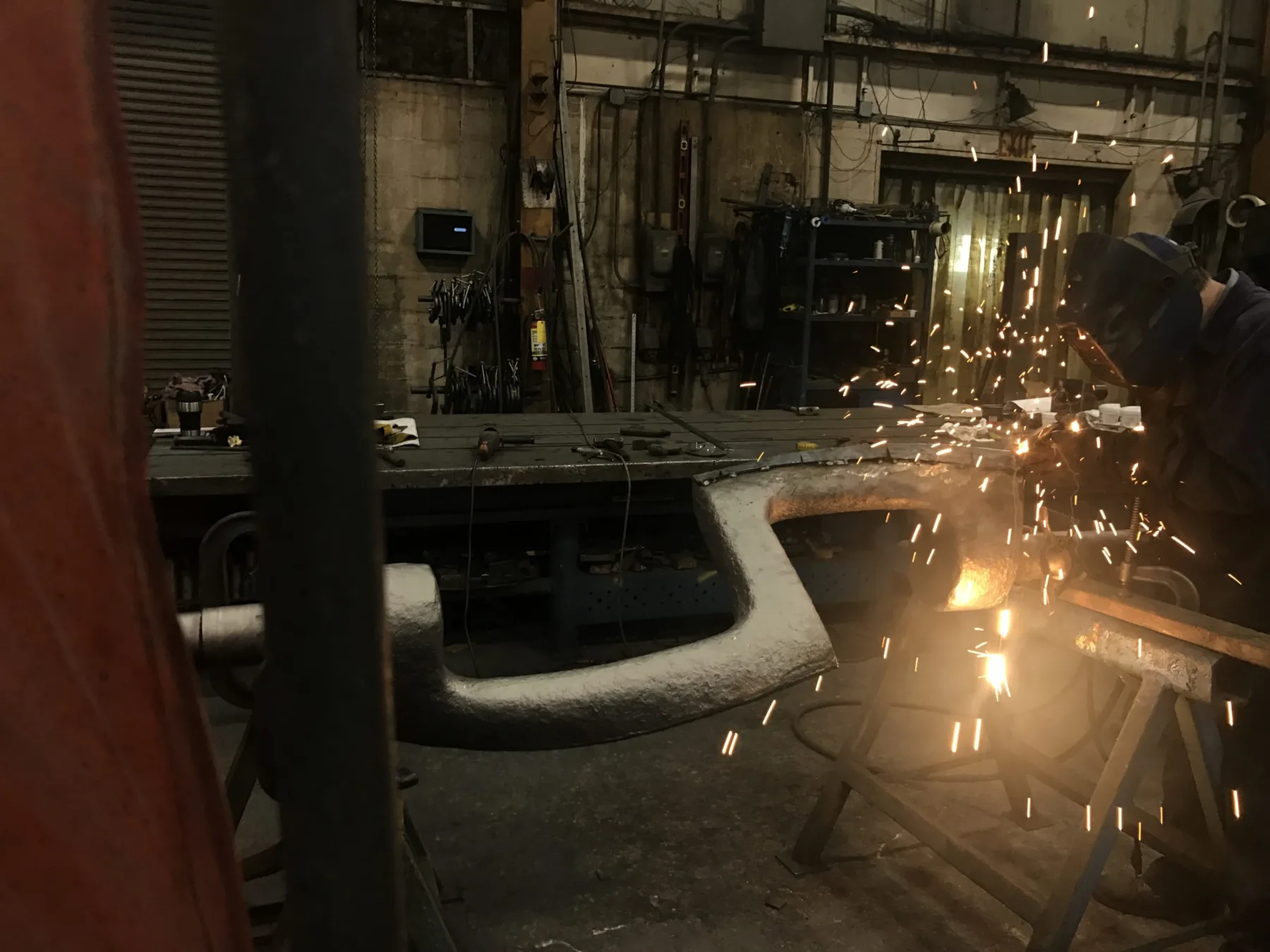 A welder rebuilding a Sigma mixer blade with sparks flying in the Gear Force Machine shop.