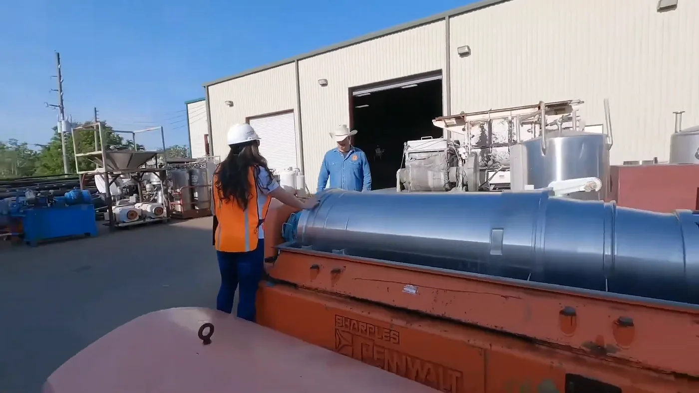 A decanter centrifuge rotating assembly on an orange skid being inspected in the yard outside an open shop bay.
