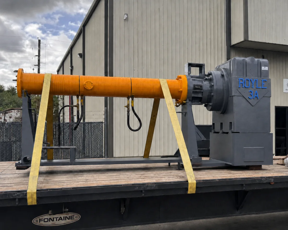 The same Royle 3A extruder gearbox and barrel fully rebuilt with fresh orange paint, strapped down on a flatbed ready to ship.
