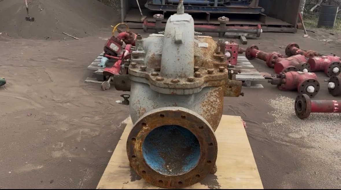 A split-case centrifugal pump as received, set on plywood in the yard with heavy rust across the suction flange and patchy corrosion over the old blue casing paint.