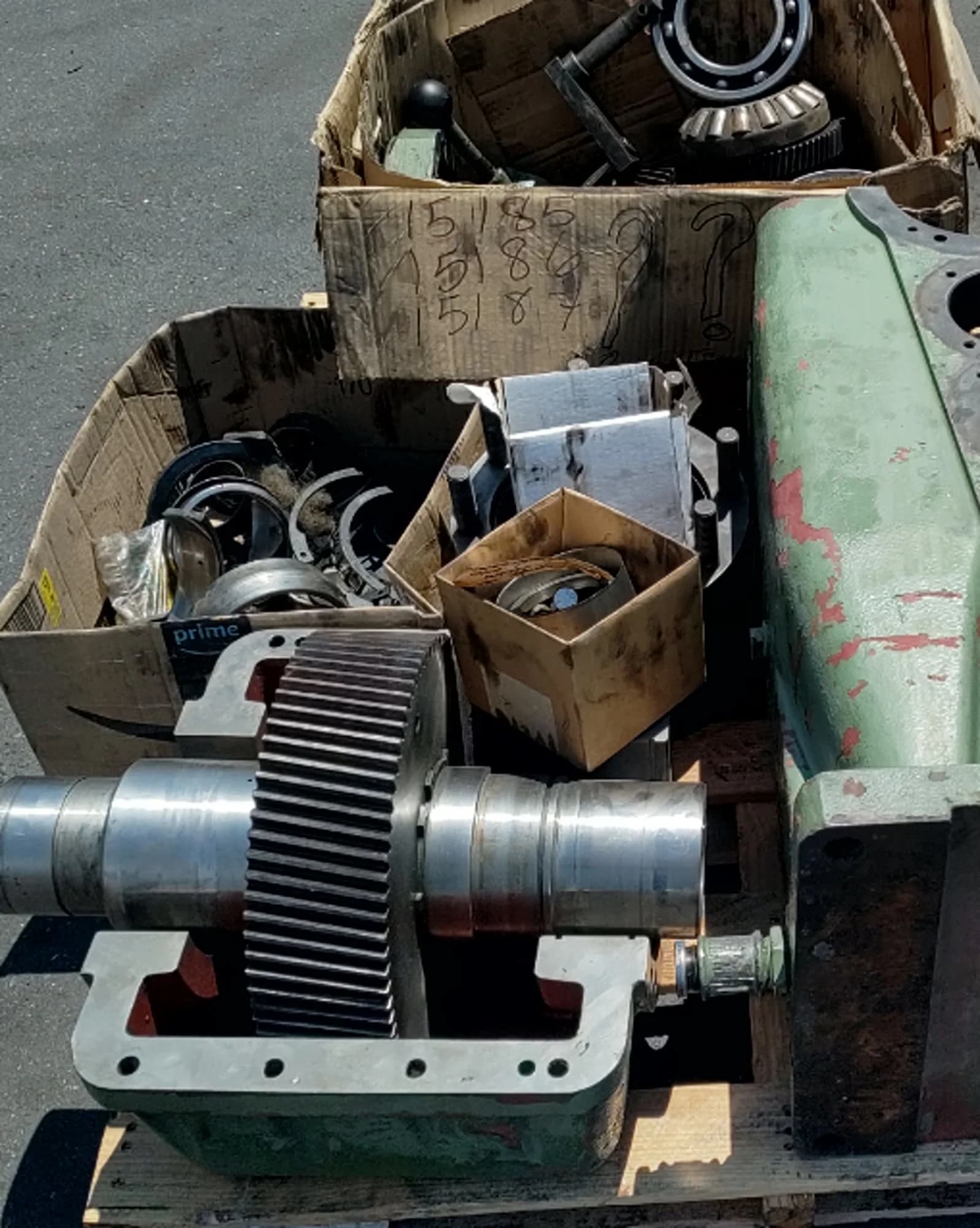 A precision-machined helical gear seated on polished bearing journals inside an open gearbox housing, with boxes of inspected bearings and hardware organized during disassembly at the Gear Force Machine shop.