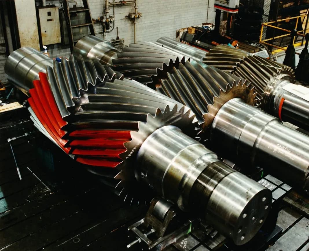 Massive herringbone gear shafts with red contact-marked teeth on the Gear Force Machine shop floor.