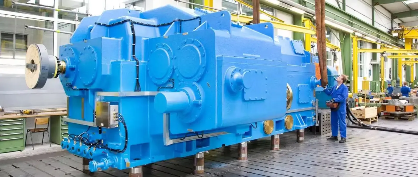 A fully rebuilt large-format extruder gearbox in blue paint, sized against a technician for scale at the Gear Force Machine shop.