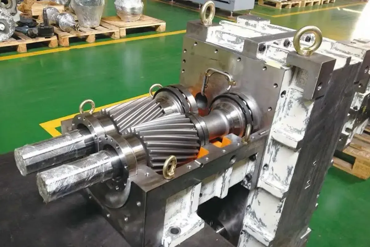 Exposed helical gear train and shafts inside an open extruder gearbox housing during reassembly.