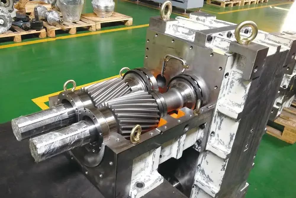 Exposed helical gear train and shafts inside an extruder gearbox, reference-measured for replacement parts.