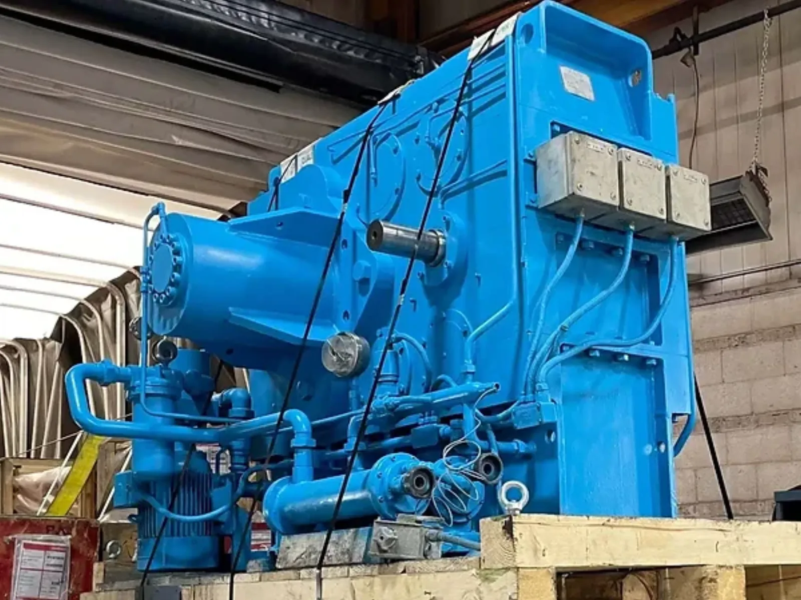 A rebuilt Pomini extruder gearbox in blue finish, suspended from a shop crane after completion.