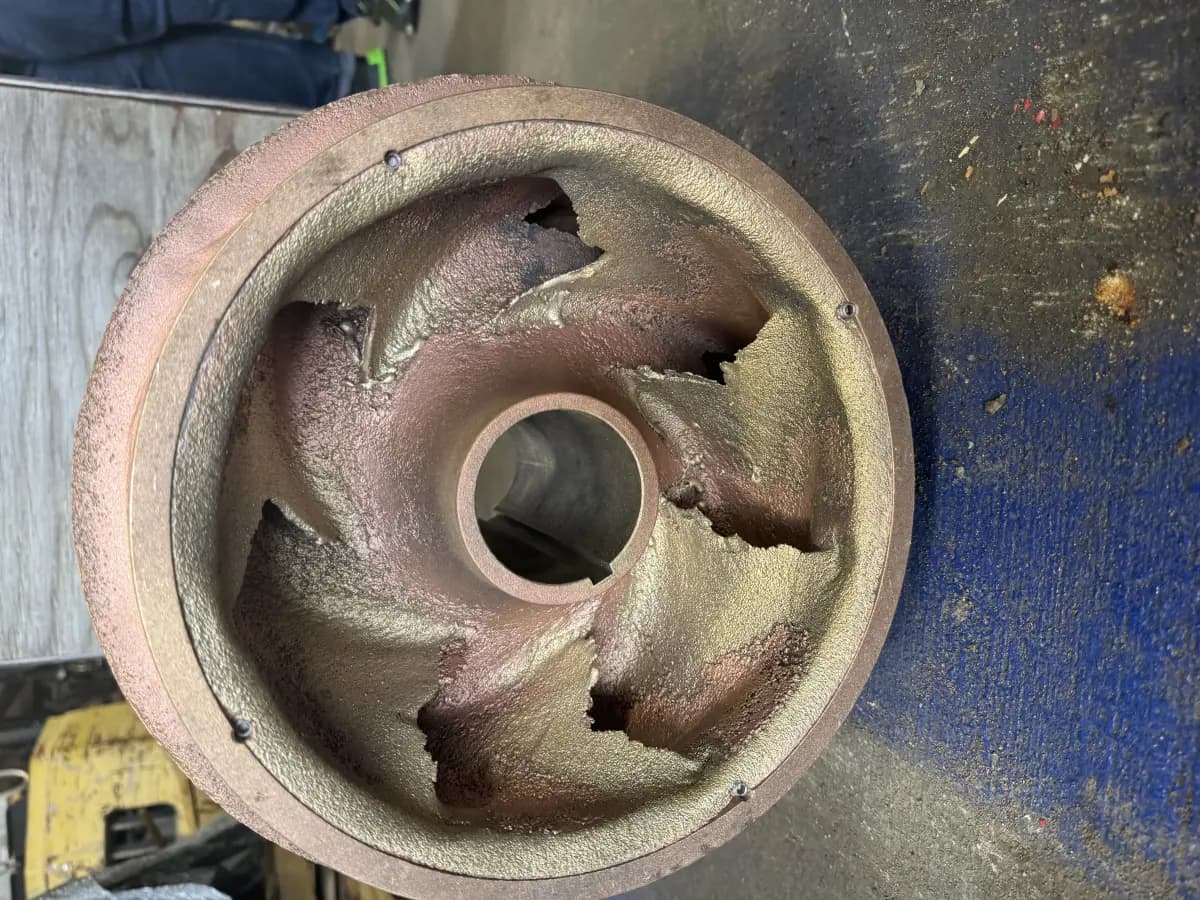 Close-up of a bronze impeller with severe cavitation and erosion damage on the vanes, documented during teardown.