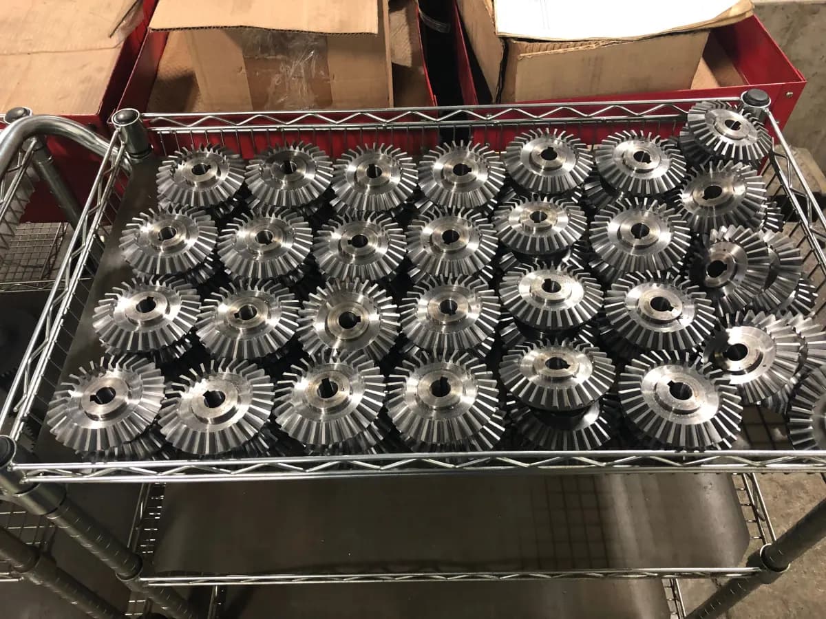 A batch of freshly cut custom bevel gears racked on a shop cart.