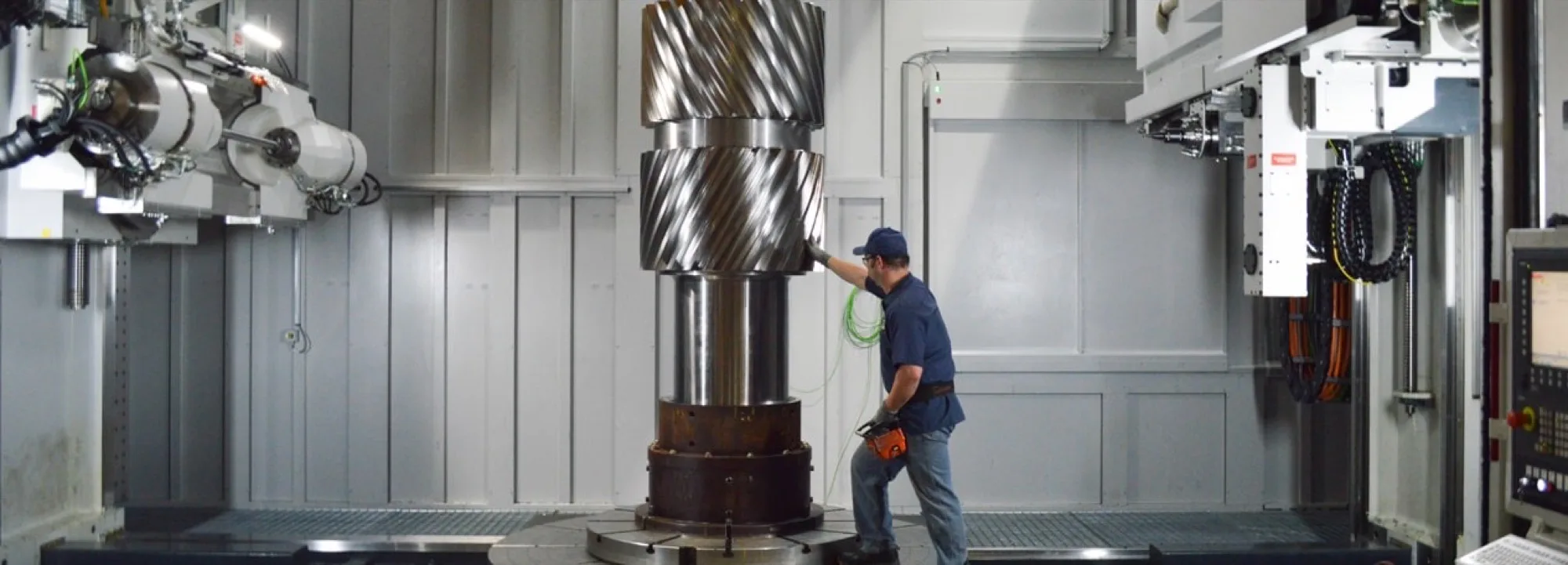 A technician measuring a large double-helical gear shaft on a horizontal mill during custom manufacturing.